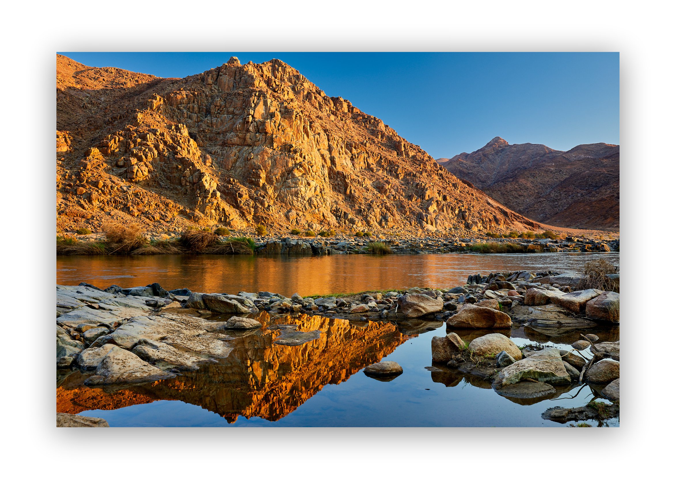 The early morning sun turns a mountain in Namibia into a golden display of symmetry captured in its reflection of the Gariep river
